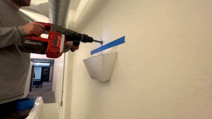 Up close photo of hammer drill being used on concrete wall with a Dust Diaper